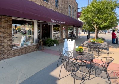 Tables and chairs line the sidewalk in front od a red brick building