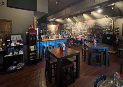 Cozy cafe interior with wooden tables and chairs, a well-lit counter, and chalkboard menus on the wall. Shelves display various items. Warm lighting creates a relaxed atmosphere.