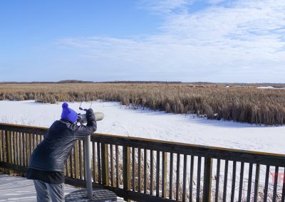 A woman dressed in winter clothes looks through a spotting scope on an observation platform on a frozen lake