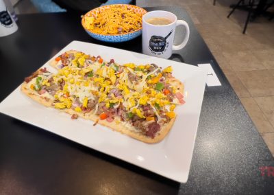 A closeup of a breakfast pizza and breakfast skillet with a coffee mug on a restaurant table
