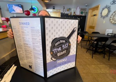 A woman sitting at a restaurant table is nearly covered by an oversized menu