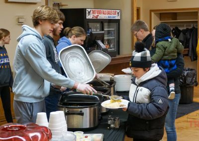 A teenage boy serves a smaller boy from a tabletop roaster at a lunch line