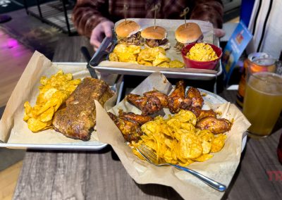 A closeup pf three platters of BBQ ribs, chicken, sandwiches, mac and sides