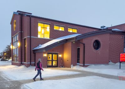 A woman walks towards a modern red brick church in the winter
