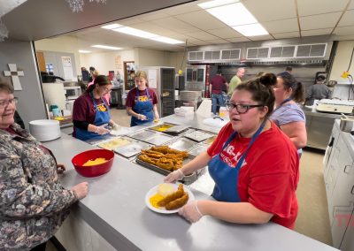 A server at a window slides a plate of fried fish across a counter to a customer