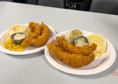 Two plates of fried fish, mashed potatoes with gravy, and corn on a table