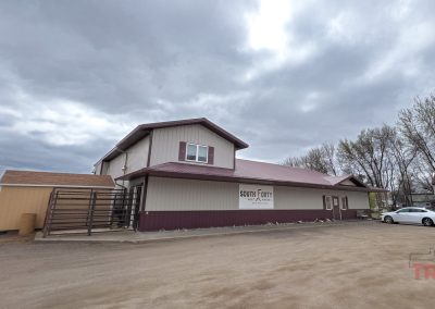 A two-story building with a red roof and beige siding sits under a cloudy sky in Lucan, MN. A sign reads South Forty Meat Market. A white car is parked nearby, and bare trees are visible in the background on the right.