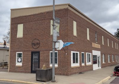 Half Pint Coffee Co is housed in a two-story brick building with cream trim on a street corner, featuring several windows and a central door. Nearby, a person is working on the roof of an adjacent building under a cloudy sky.
