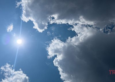 The sun shines brightly in a blue sky partially covered by large, fluffy white clouds.