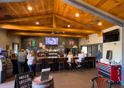 A cozy bar in Battle Lake, MN, with a wooden vaulted ceiling, patrons at the bar, multiple TVs on the wall, beer taps behind the counter, and an ABC Brewing chalkboard sign welcoming customers near the entrance.