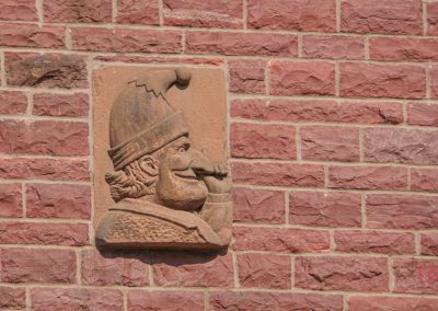 A carved stone plaque in Pipestone MN shows a jester in a pointed hat in profile. Mounted on a red brick wall, its an intriguing stop on any local History Walk.