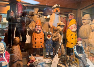 A collection of carved wooden sailor figurines, some painted in yellow raincoats and hats, displayed behind glass with visible price tags. Other wooden figures and carvings are also in the display case.