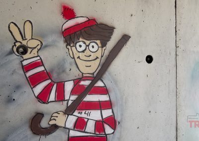 Graffiti art of the character Waldo in a red-and-white striped shirt and hat, glasses, and holding a cane, flashing a peace sign. #41 is written on the shirt.