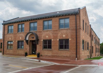 A two-story brick building with large windows and an arched entrance labeled HISTORY CENTER, situated on a wet street corner under a cloudy sky.