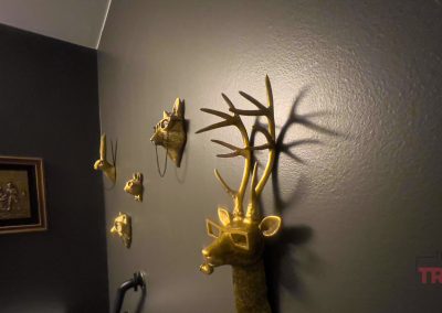 Gold animal head wall sculptures, including a deer with glasses, are mounted on a dark gray wall. A framed artwork hangs nearby.