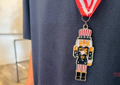 Close-up of a person wearing a medal with a nutcracker figure dressed in a patriotic Uncle Sam outfit, hanging from a red, white, and blue ribbon. The person is wearing a dark blue shirt.