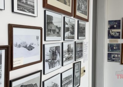 A wall displays an arrangement of framed black-and-white and color photographs depicting historical buildings and scenes. Some captions are visible, and a Minnesota Trails logo is seen in the bottom right corner.