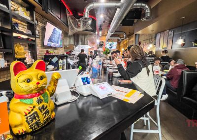 A bustling Boil Seafood Restaurant interior in Saint Cloud MN, with people seated at the bar and tables. A large golden maneki-neko figurine and a Grubhub pickup sign sit on the counter amid modern decor and bright lighting.